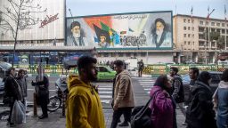 Iranian people walk along the streets in Tehran, Iran, on February 24, 2024. A mural on Enqelab Avenue features the supreme leader of Iran Ali Khamenei, left, soldier Hossein Fahmideh, and the spiritual leader of the Iranian revolution Ayatollah Khomeini.