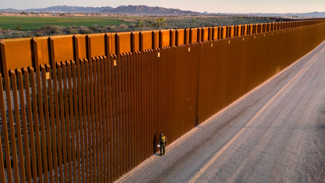 In an aerial view, a US Border Patrol agent searches for immigrant footprints while looking through the US-Mexico border fence on March 9, in Yuma, Arizona.