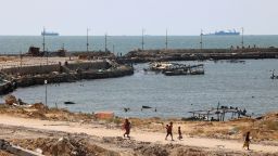 Palestinians walk past a jetty in Gaza City with a view of navy vessels off the coast as part of a humanitarian "maritime corridor" announced by US Central Command on May 17. The US military said aid deliveries began on May 17 via a temporary pier in Gaza aimed at ramping up emergency humanitarian assistance to the war-ravaged Palestinian territory.