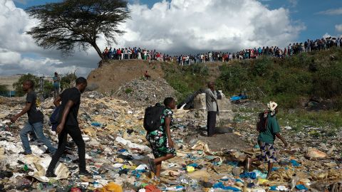 People walk among rubbish as others stand on the edge of a dumpsite where six bodies were found at the landfill in Mukuru slum, Nairobi, on July 12, 2024.