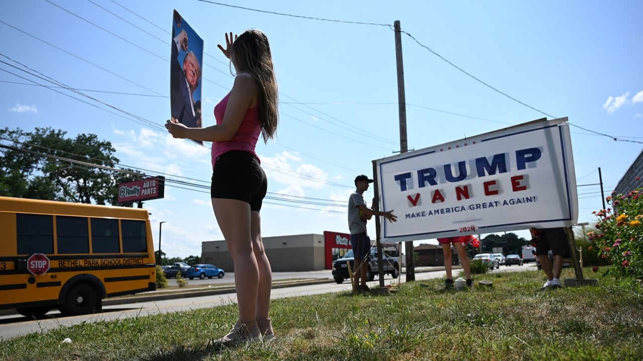 Julianna Grooms holds a photo of former President Donald Trump as neighbors help she and her mother secure a Trump yard sign that they used tape to add the name of Trump's running mate J.D. Vance outside their home on July 16, 2024, in Bethel Park, Pennsylvania.