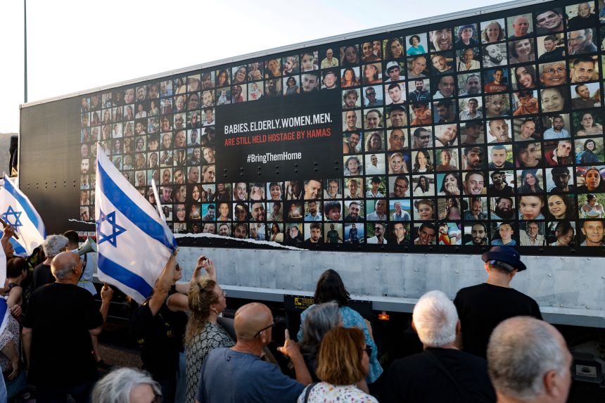 People stand near a wall covered with pictures of Israeli hostages during a demonstration against the Israeli government in the northern Israel city of Karmiel on July 25, 2024.