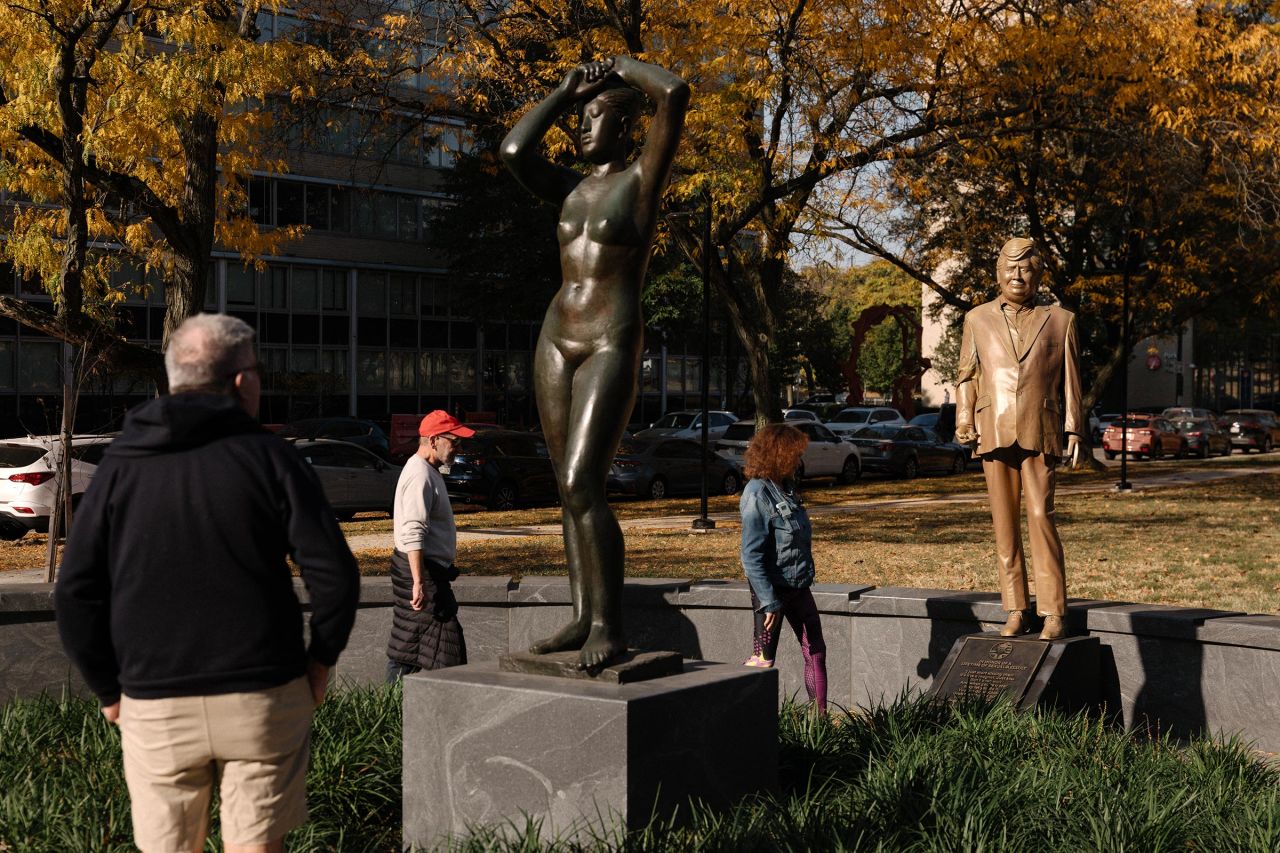 Pedestrians look at a statue of Donald Trump behind Gerhard Marcks' sculpture Maja, in Maja Park in Philadelphia.