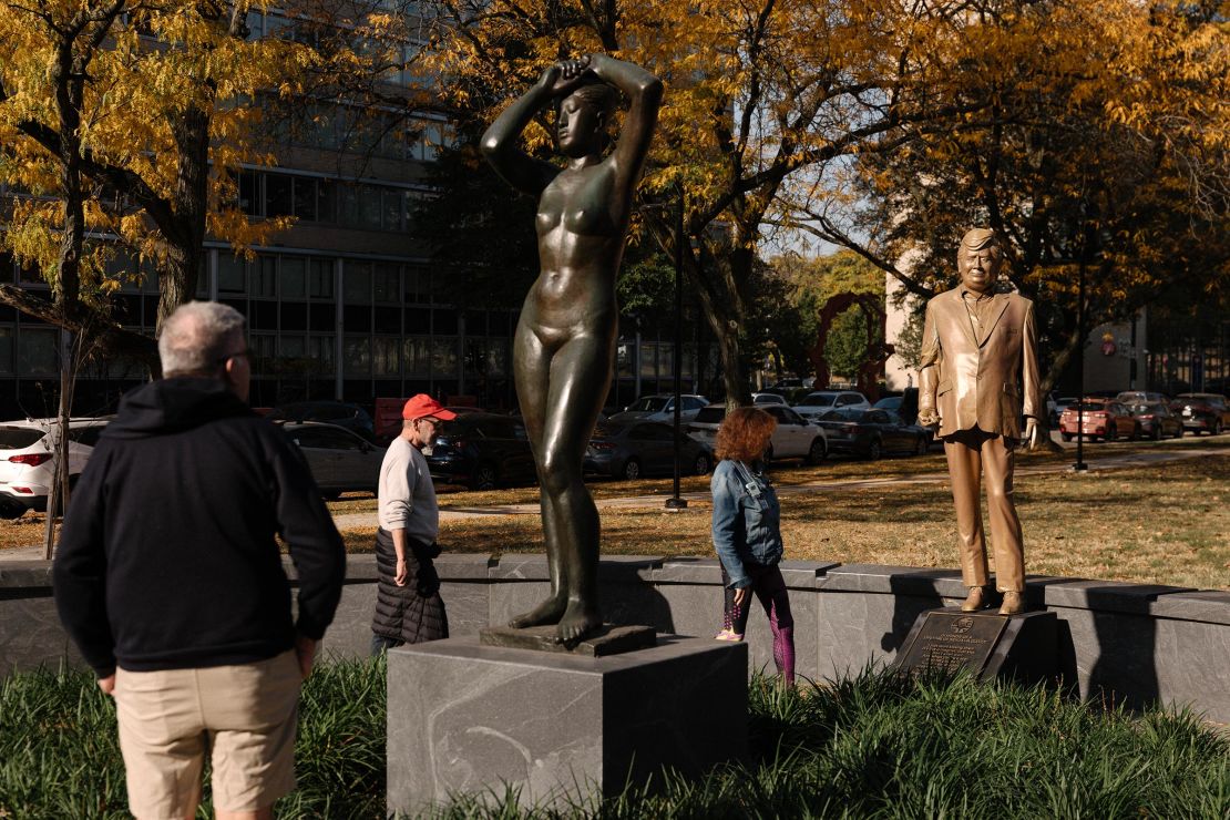 Pedestrians look at the Donald Trump statue behind Gerhard Marx's Macha sculpture in Maya Park in Philadelphia.