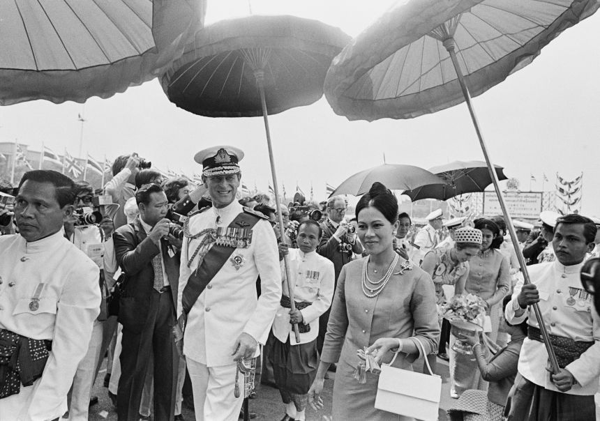 Prince Philip walks with Queen Sirikit during the royal tour to Thailand on February 16, 1972. Princess Anne can be seen receiving a gift in the background.