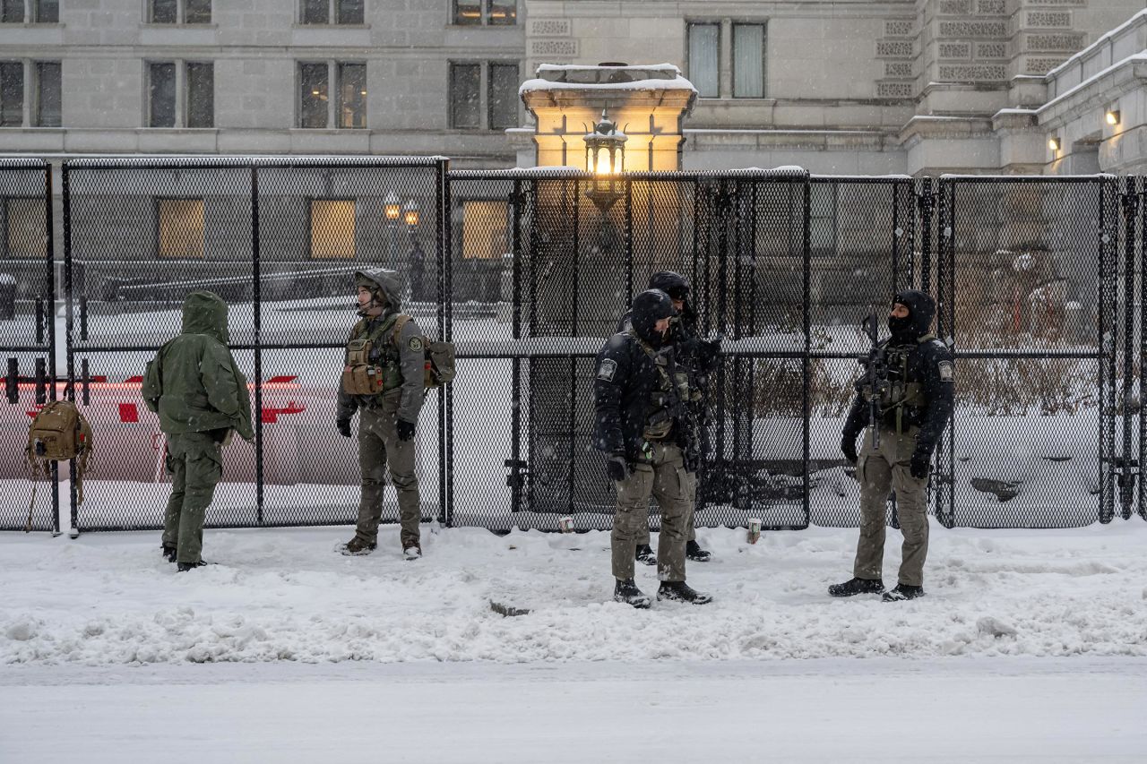 Members of law enforcement stand on guard near the fencing surrounding the US Capitol during a snow storm on January 6 in Washington, DC. 