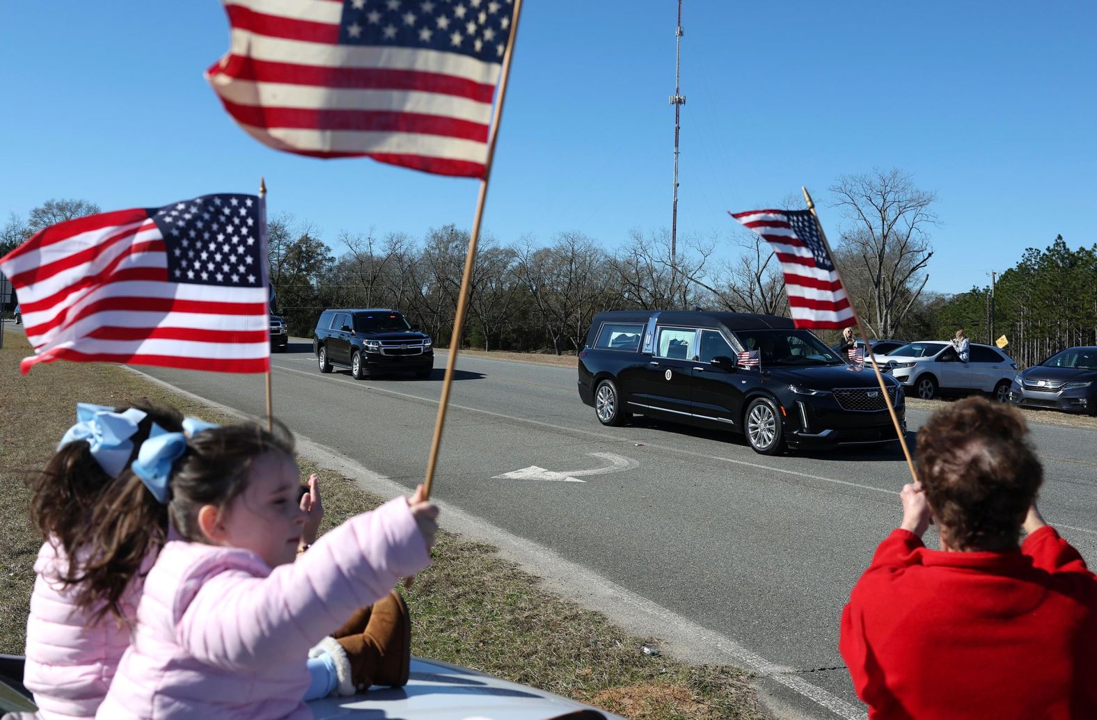 Mourners line the street and wave flags as former US President Jimmy Carter's hearse passes by on January 4, 2025 in Plains, Georgia.