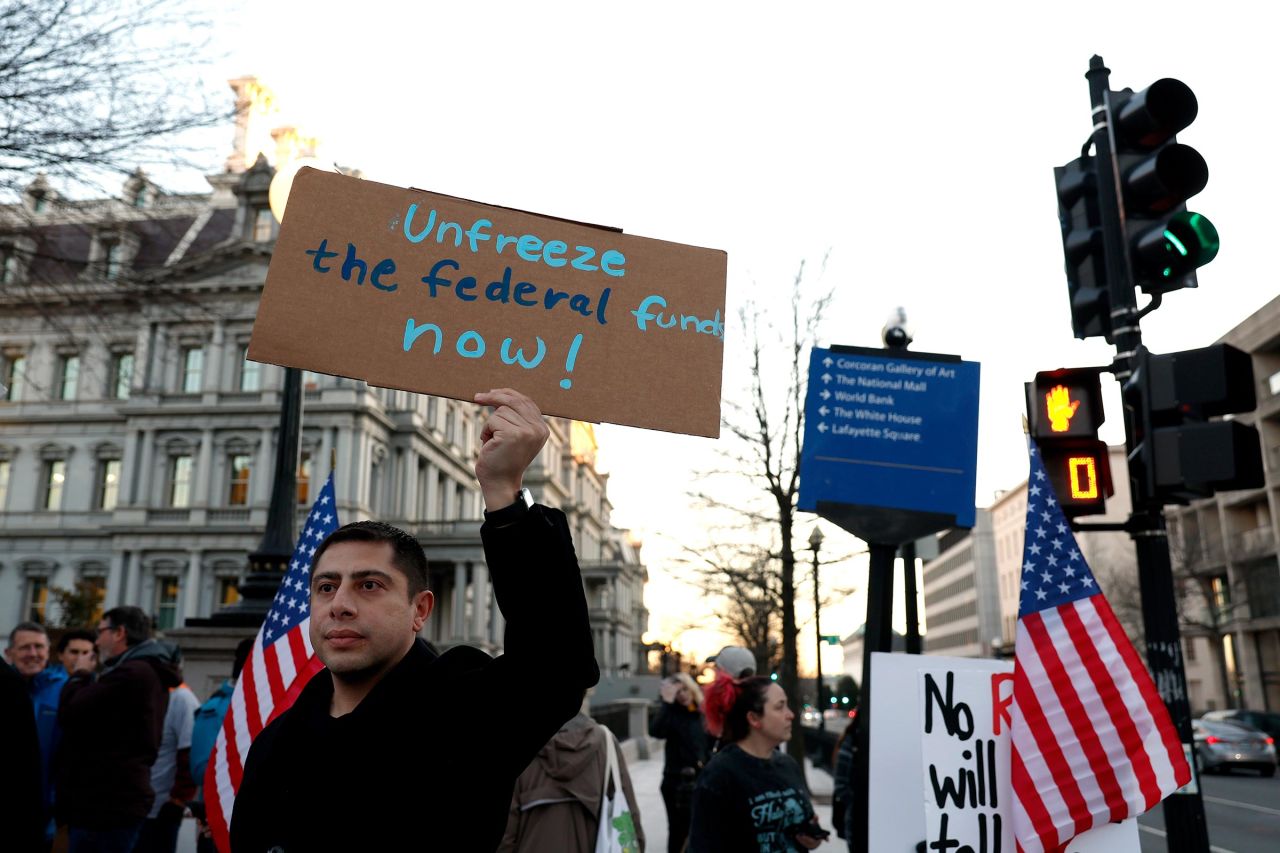 An activist protests against President Donald Trump's plan to stop most federal grants and loans during a rally near the White House on January 28, 2025 in Washington, DC. 