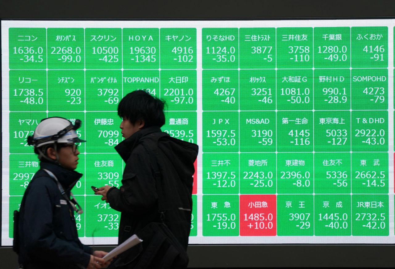 Pedestrians walk past an electronic board showing the Nikkei 225 index on the Tokyo Stock Exchange along a street in central Tokyo on February 3.