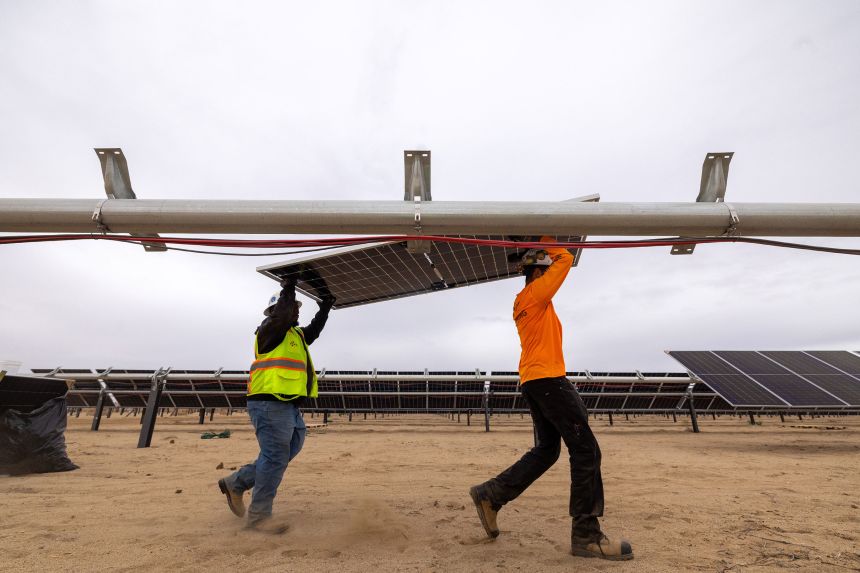 Workers install solar panels for the Los Angeles Department of Water and Power's biggest solar and battery storage plant, the Eland Solar and Storage Center in the Mojave Desert of Kern County, on November 25, 2024, near California City, California.