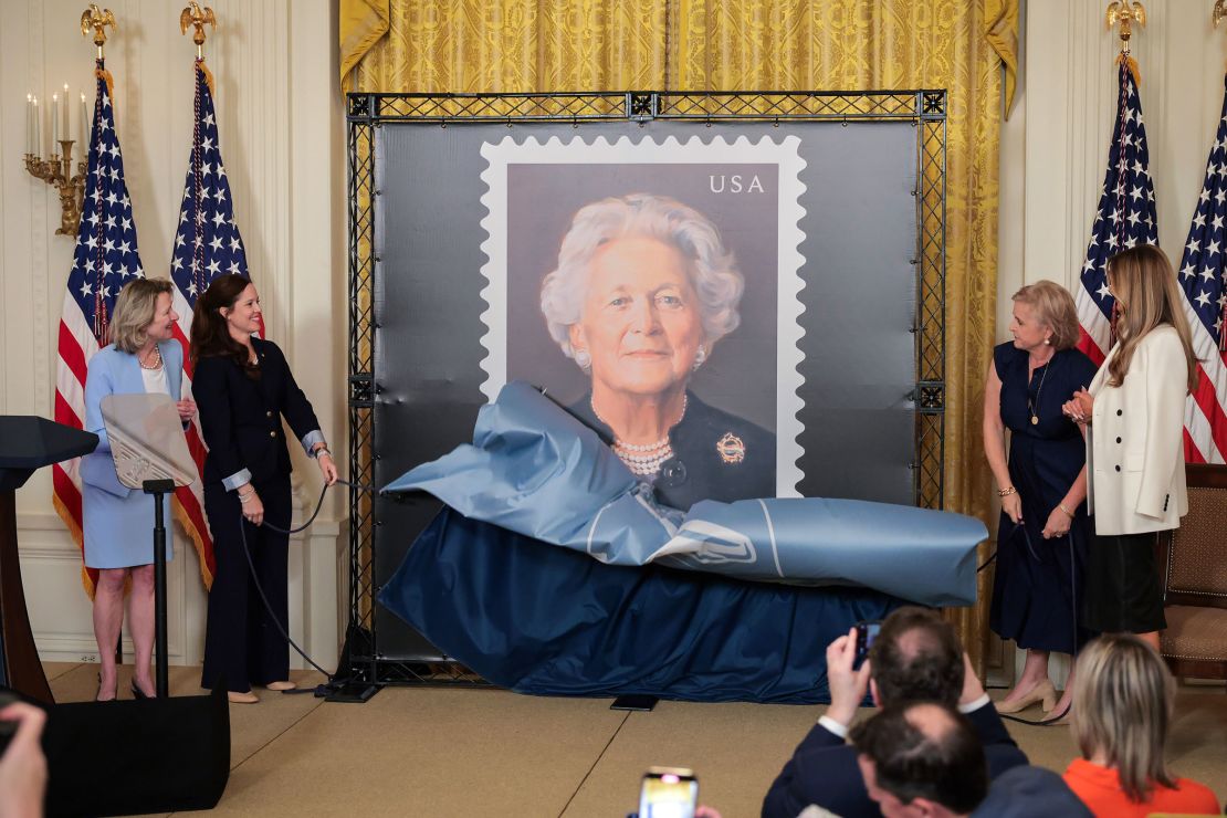 Vice President of corporate affairs of the US Postal Service Judy de Torok, CEO of the George & Barbara Bush Foundation Alice Gonzalez Yates, daughter of Barbara Bush Dorothy Bush Koch, and first lady Melania Trump unveil the US Postal Service stamp honoring former first lady Barbara Bush in the East Room at the White House on May 8 in Washington, DC.