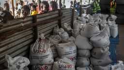 Congolese refugees look through a corrugated metal fence at the final batches of food delivered by the now-dismantled United States Agency for International Development (USAID) in a storage and food delivery area at the Musenyi refugee site in Giharo, on May 7.