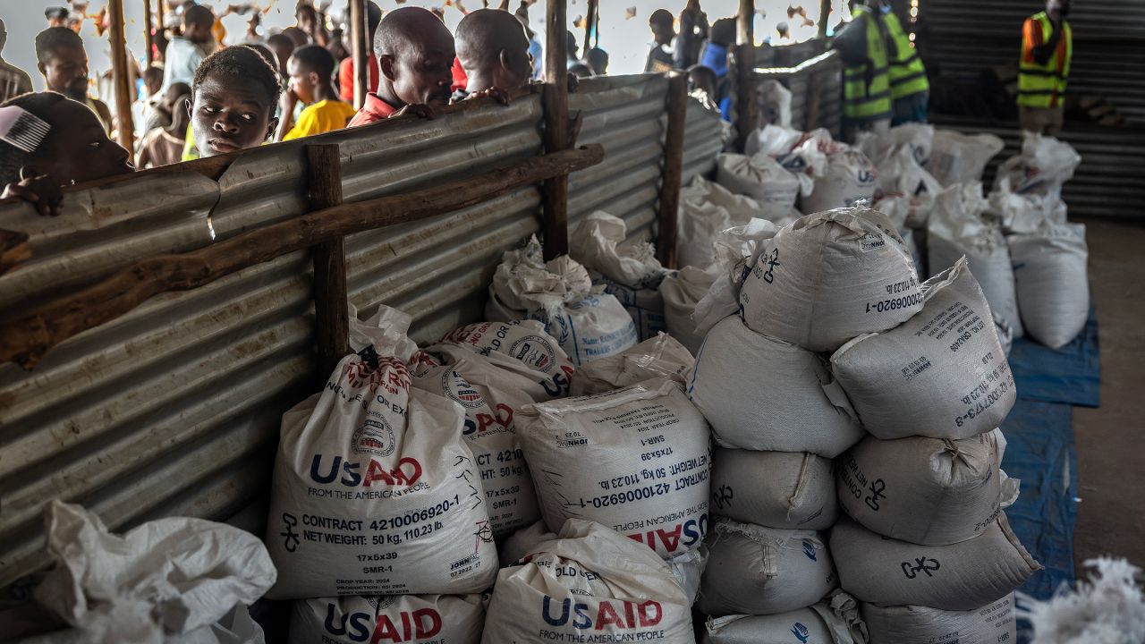 Congolese refugees look through a corrugated metal fence at the final batches of food delivered by the now-dismantled United States Agency for International Development (USAID) in a storage and food delivery area at the Musenyi refugee site in Giharo, on May 7.