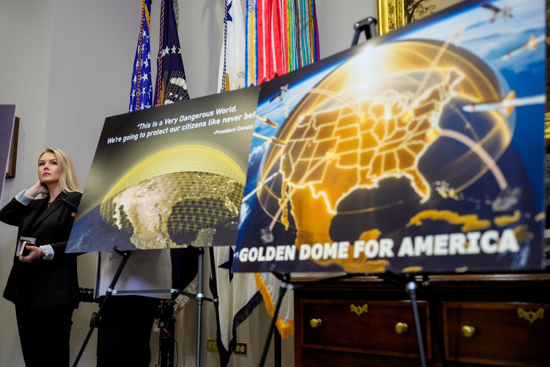 White House Press Secretary Karoline Leavitt looks on from behind posters depicting a