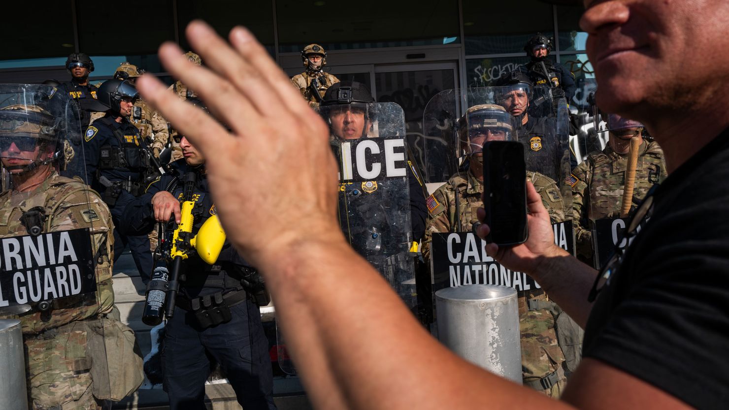 A person holds up their phone in front of the National Guard and police as they confront protesters following three days of clashes with police after a series of immigration raids on June 9, in Los Angeles.