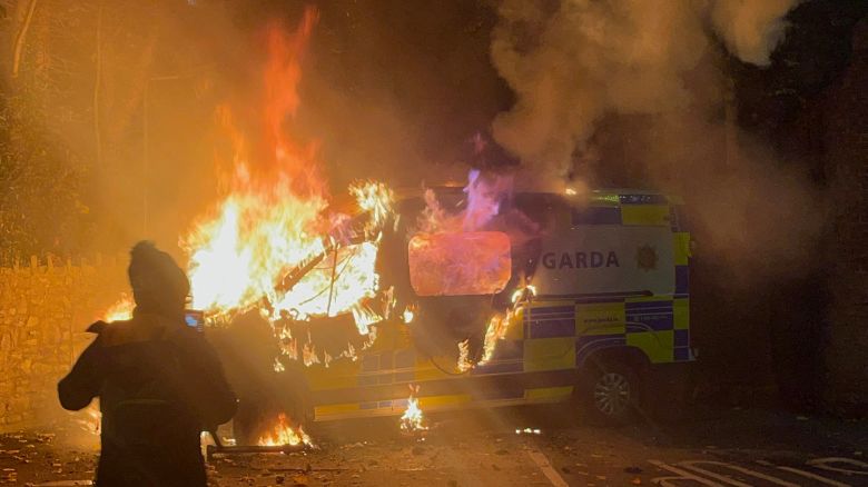Onlookers film a police vehicle burning as a demonstration outside a hotel housing asylum seekers turns violent in Saggart, south-west of Dublin in Ireland on October 21, 2025. Police in riot gear clashed with at least 500 protesters in Dublin on Tuesday outside an asylum seeker hotel, following allegations that a 10-year-old girl was sexually assaulted.