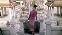Queen Sirikit of Thailand, standing before a porcelain encrusted tower in one of the many pavilions of the Grand Palace, wearing a Thai silk pa-hom and pa-noong, in gold, red, and pink. (Photo by Henry Clarke/Condé Nast via Getty Images)