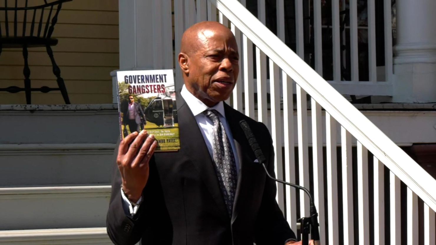 New York City mayor Eric Adams speaks to the media outside Gracie Mansion after a judge dismissed charges against him, holding up a book written by FBI Director Kash Patel.