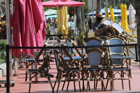 An employee at the Clevelander bar and restaurant on Ocean Drive stacks chairs after they shut down due to public health concerns caused by COVID-19 on Monday, July 13, 2020, in Miami Beach, Florida.