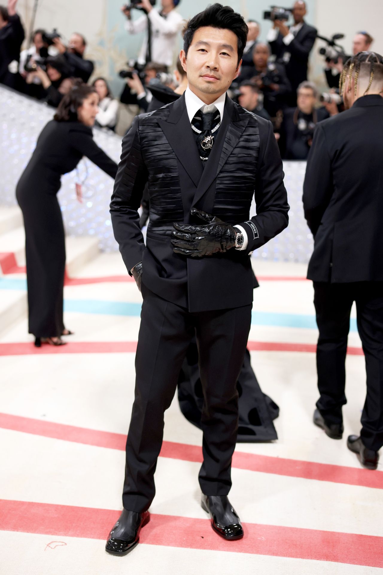 Simu Liu's black gloves and tie adorned with a silver brooch pay homage to the iconic designer.