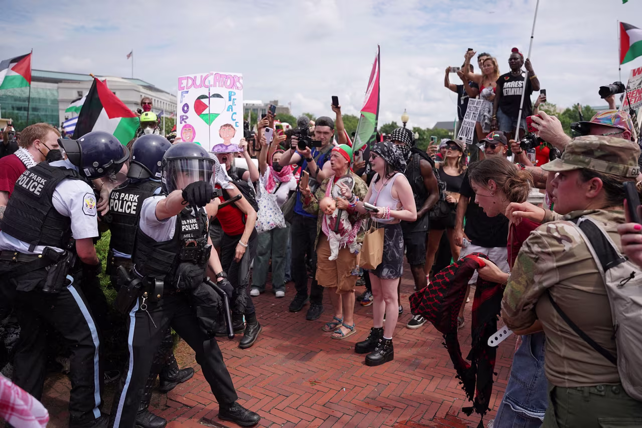 US Park Police officer gestures with pepper spray while other officers carry away a handcuffed demonstrator.