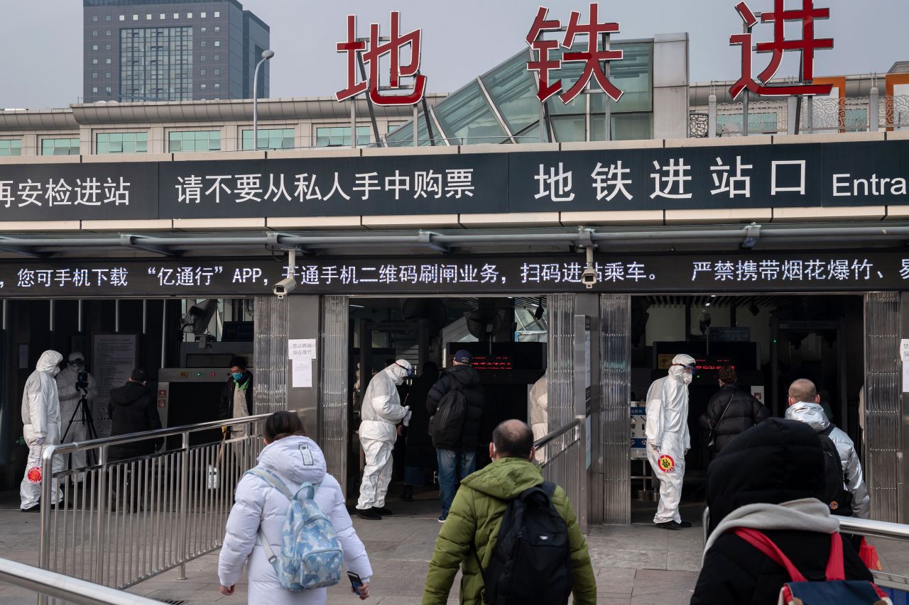 Security personnel wearing protective clothing check the temperature of people using portable devices and an advanced thermo camera (L) at a subway station entrance in Beijing on January 27.