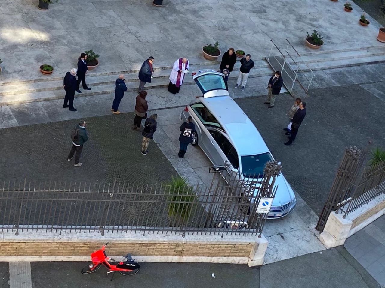 A priest comes out of a church in Rome to give a blessing over a coffin sitting in the trunk of a car.