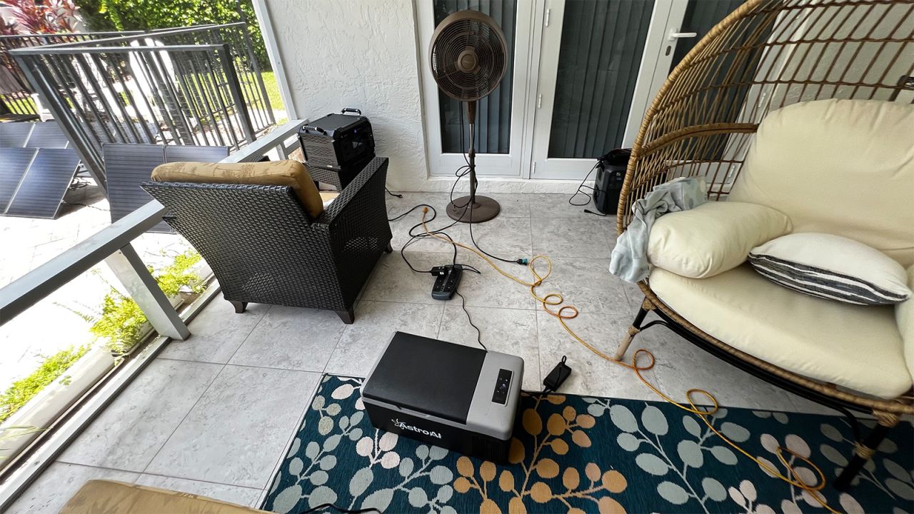 A solar generator set up on a patio, with multiple cable runs visible between patio furniture as well as an Astro refrigerator