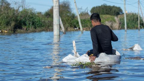Un joven sentado en una bolsa de piedras contempla hasta donde llegó el agua de las inundaciones frente a su hogar.