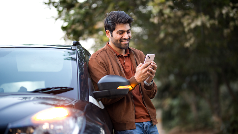 Man leans on a car while looking at a cellphone.