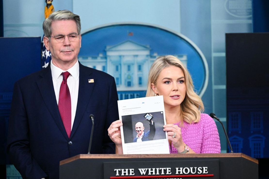 La secretaria de prensa de la Casa Blanca, Karoline Leavitt, acompañada por el secretario del Tesoro, Scott Bessent, sostiene un artículo de noticias sobre el CEO de Amazon, Jeff Bezos, durante la sesión informativa diaria en la Sala de Prensa Brady de la Casa Blanca el 29 de abril.