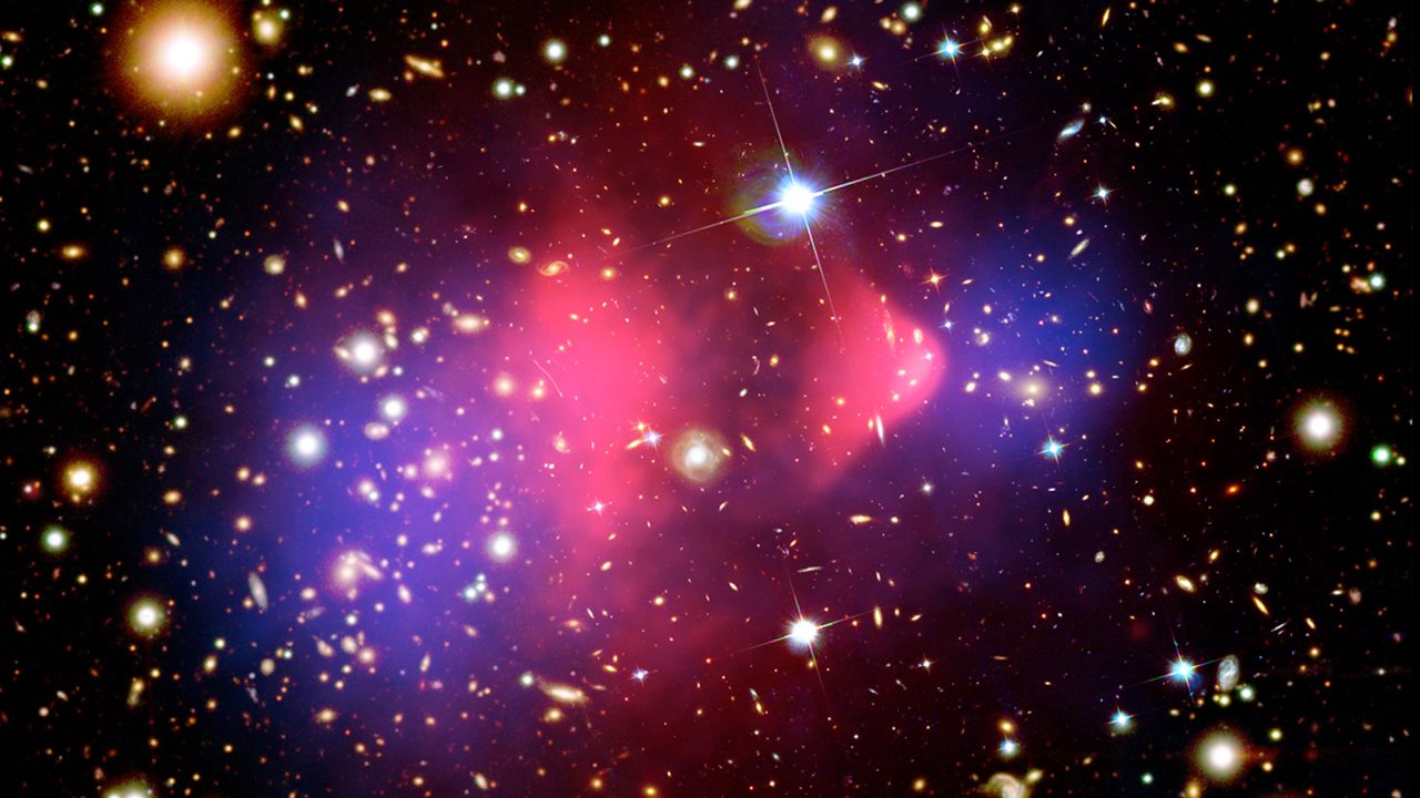 This composite image shows the galaxy cluster 1E 0657-56, also known as the "bullet cluster." This cluster was formed after the collision of two large clusters of galaxies, the most energetic event known in the universe since the Big Bang. Hot gas detected by Chandra in X-rays is seen as two pink clumps in the image and contains most of the "normal," or baryonic, matter in the two clusters. The bullet-shaped clump on the right is the hot gas from one cluster, which passed through the hot gas from the other larger cluster during the collision. An optical image from Magellan and the Hubble Space Telescope shows the galaxies in orange and white. The blue areas in this image show where astronomers find most of the mass in the clusters. The concentration of mass is determined using the effect of so-called gravitational lensing, where light from the distant objects is distorted by intervening matter. Most of the matter in the clusters (blue) is clearly separate from the normal matter (pink), giving direct evidence that nearly all of the matter in the clusters is dark. 