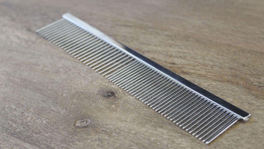 A steel dog comb on a wooden surface.