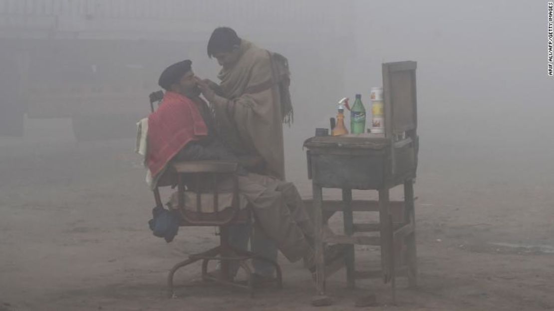 Un barbero paquistaní afeita a un cliente en la calle en medio del esmog en Lahore.