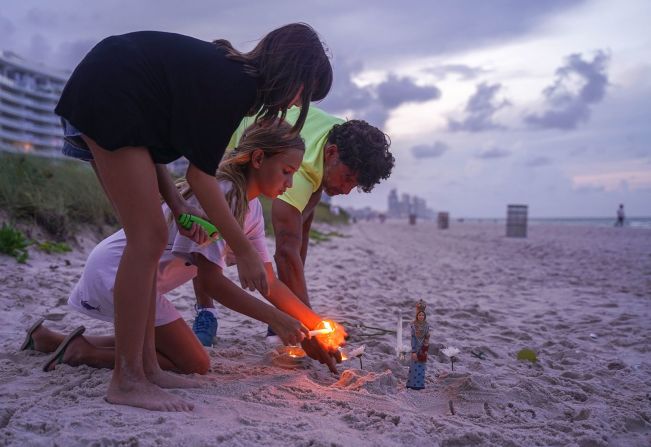 Dos personas encienden velas en la playa cerca del edificio en Surfside, Florida.