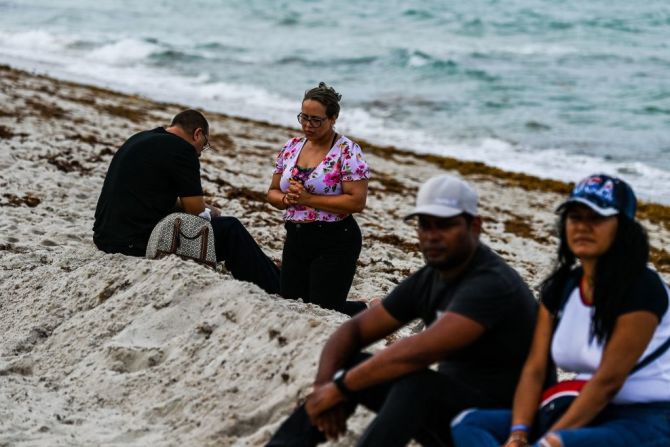 Una mujer reza de rodillas en la playa mientras avanzan las labores de búsqueda de los cuerpos de socorro.