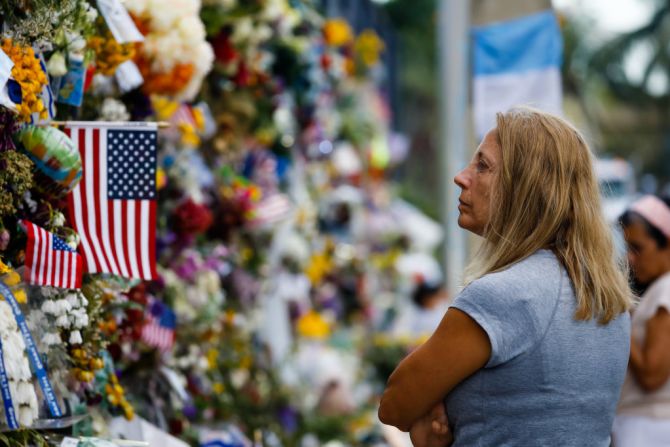 Una mujer mira el monumento repleto de flores levantado en el lugar.