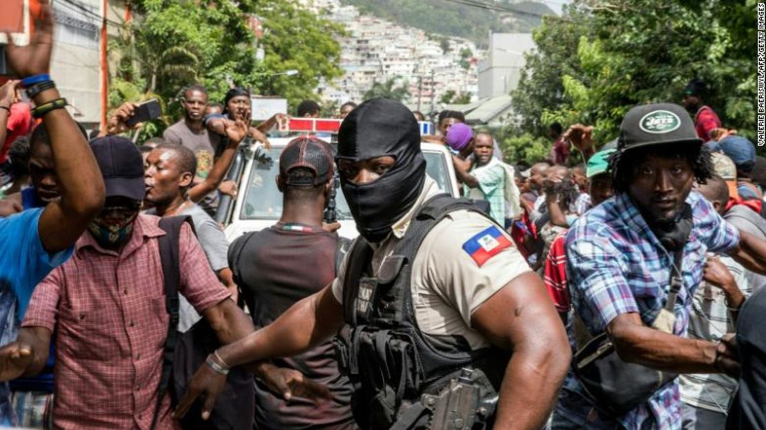 Gente vitorea mientras un vehículo de la policía pasa por delante de la comisaría en la que desde el 8 de julio se encuentran detenidos hombres a quienes se les acusa de estar involucrados en el asesinato del presidente Jovenel Moïse, en Puerto Príncipe.