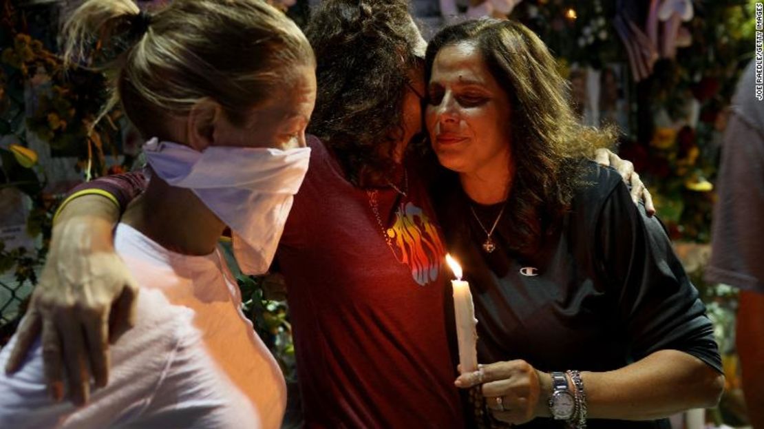 Michelle D'Antuono, Dana Kulvin y Soraya Batista se abrazan mientras visitan el homenaje que tiene fotos de algunas de las víctimas del edificio de condominios Champlain Towers South, que se derrumbó parcialmente.