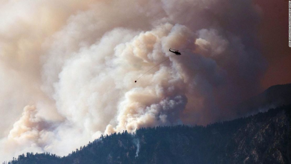 Un helicóptero se prepara para lanzar una bomba de agua mientras el humo se extiende a lo largo del valle del río Fraser, cerca de Lytton, Columbia Británica, Canadá, el viernes 2 de julio de 2021.