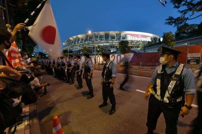 Agentes de policía montan guardia frente a personas que se reúnen fuera del Estadio Olímpico antes de la ceremonia de apertura de los Juegos Olímpicos de Tokio 2020.