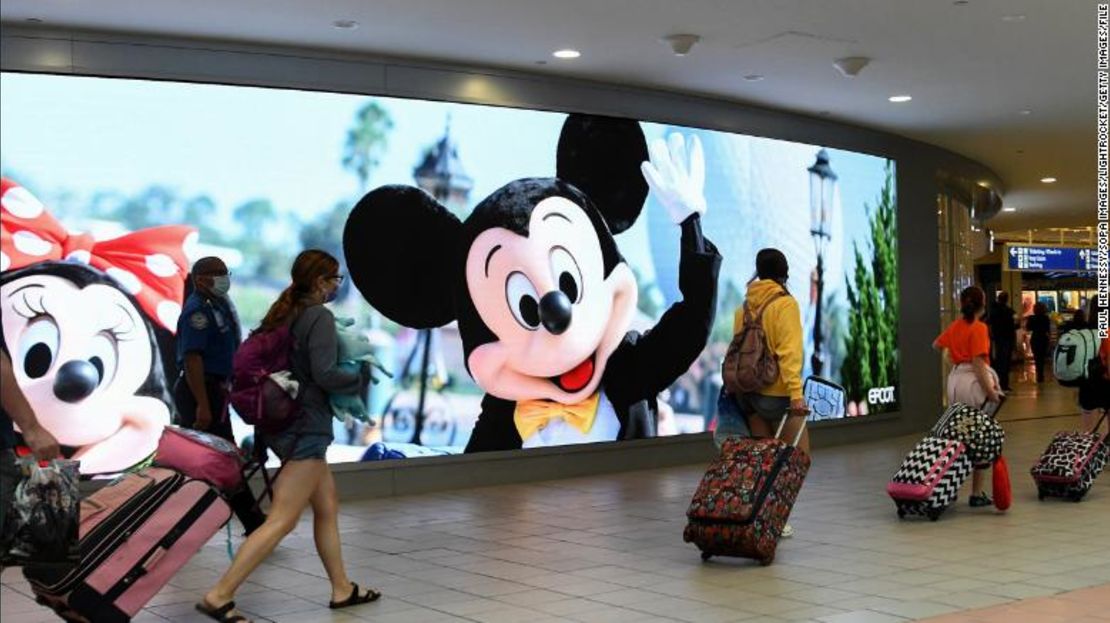 iajeros pasan junto a un letrero que anuncia Walt Disney World en el Aeropuerto Internacional de Orlando, el 2 de julio de 2021.