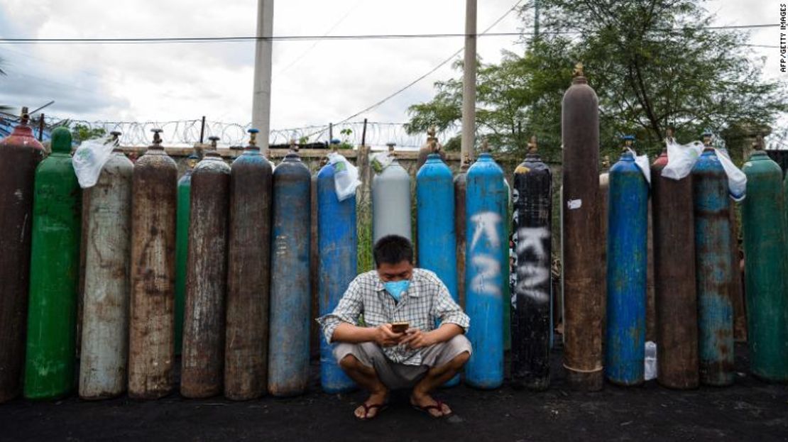 Un hombre usa su teléfono móvil frente a botes de oxígeno vacíos fuera de una fábrica en Mandalay, el 13 de julio.