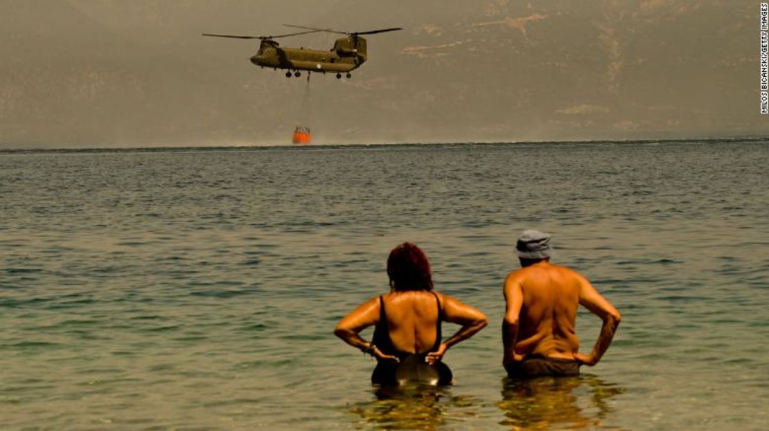 Residentes observan cómo un helicóptero Chinook del Ejército griego recoge agua mientras los bomberos continúan atacando un incendio forestal cerca de la aldea griega de Lambiri, el domingo.