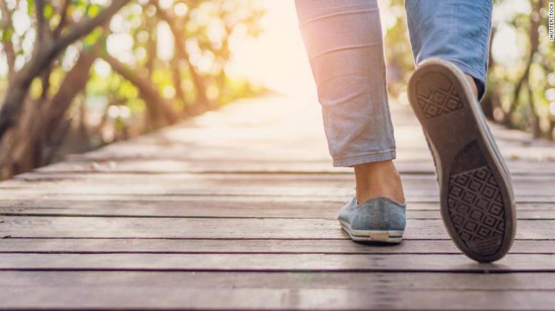 Woman is walking on small wood bridge to nature walk way with sunlight flare background.