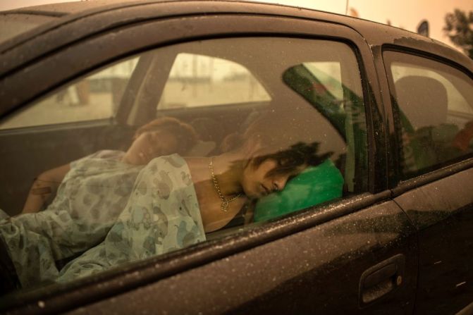 Una mujer duerme en su auto mientras las llamas consumen el pueblo de Pefki, en la isla de Evia.