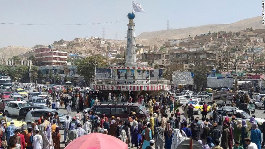 Una bandera talibán se ve en un pedestal con personas reunidas alrededor de la plaza principal de la ciudad en Pul-e-Khumri el 11 de agosto de 2021 después de que los talibanes capturaron Pul-e-Khumri, la capital de la provincia de Baghlan.