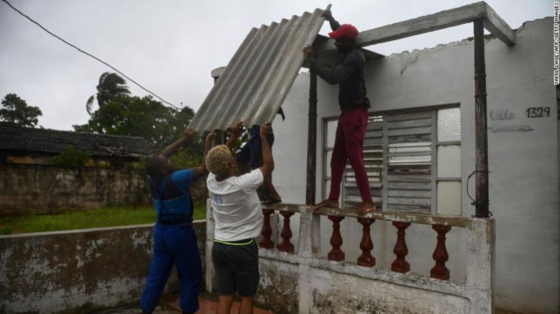 Hombres colocan una lámina de metal corrugado en el techo de una casa bajo la lluvia en Batabano, provincia de Mayabeque, a unos 60 km al sur de La Habana, el 27 de agosto de 2021, cuando el huracán Ida pasa por el este de Cuba.