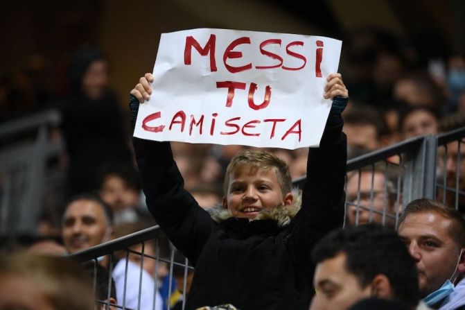 Un joven aficionado sostiene un cartel que dice "Messi, tu camiseta" durante el partido.