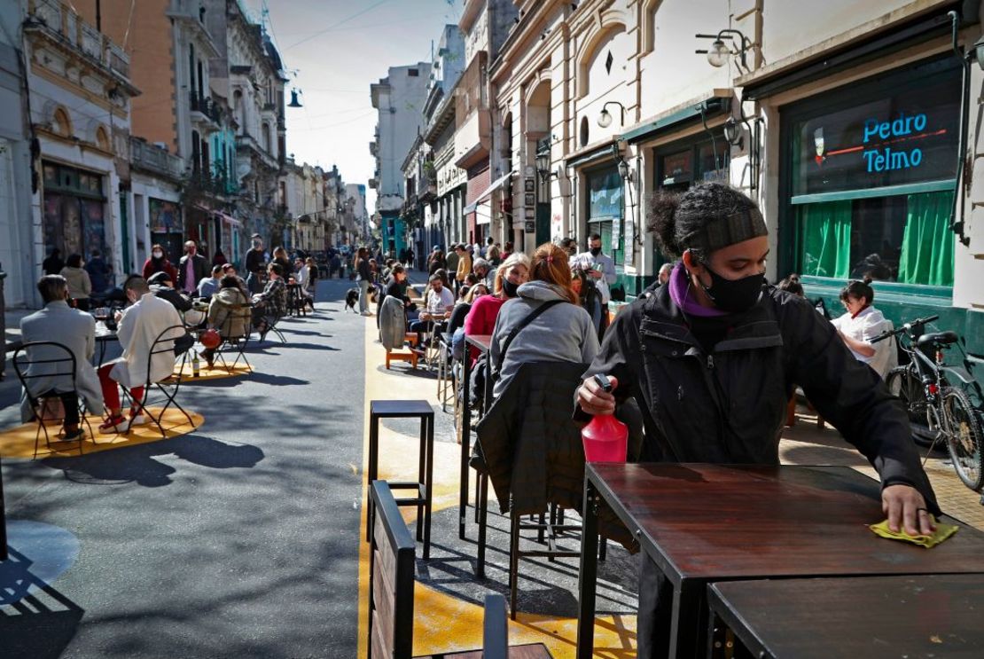 Los clientes se sientan en mesas colocadas fuera de un bar mientras un empleado limpia una mesa en el barrio de San Telmo, en Buenos Aires.